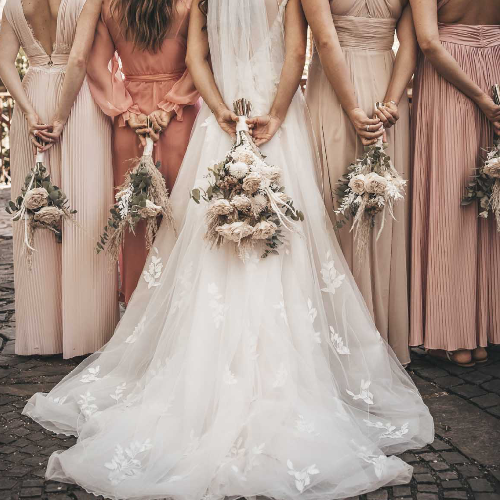 Braut und Brautjungfern mit Blumensträußen hinter dem Rücken