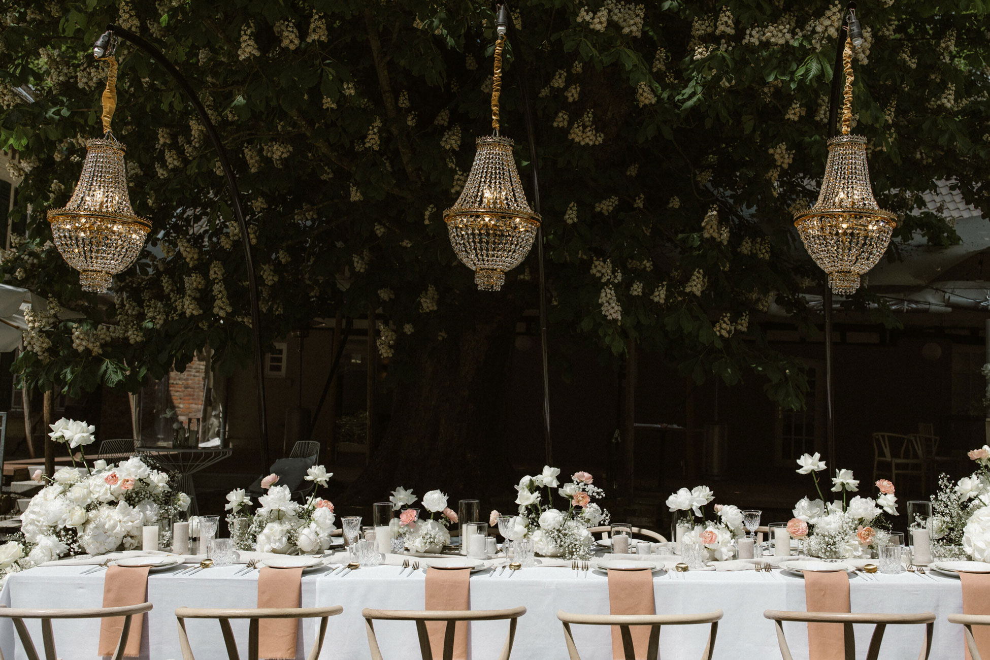 Goldenen Kristallkronleuchter hängen von von einem Baum über einem weißen Hochzeitstisch in Köln