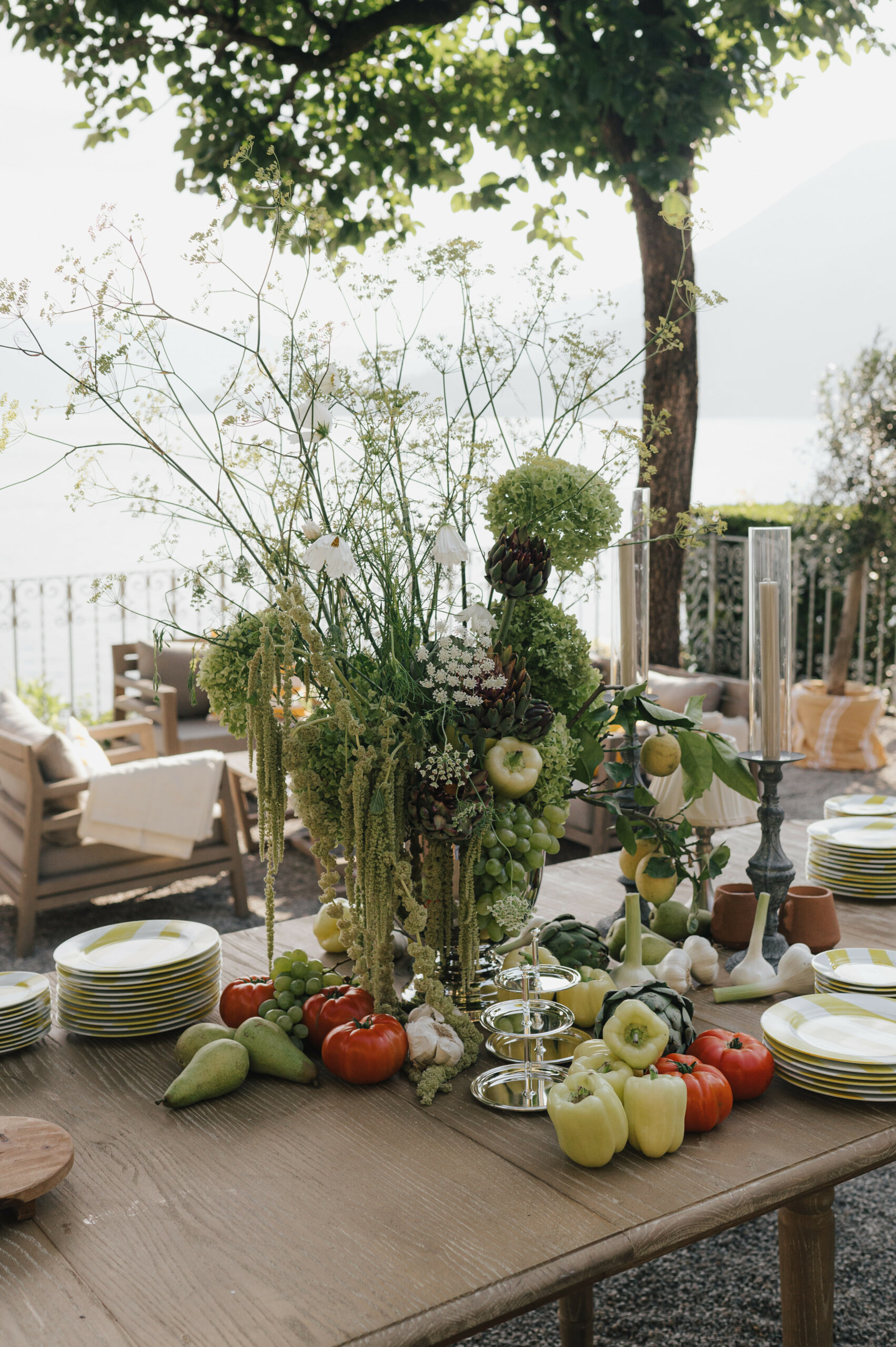 Elegante Tischdekoration mit frischem Gemüse und Blumen auf einer Terrasse in Italien mit Blick auf einen See.