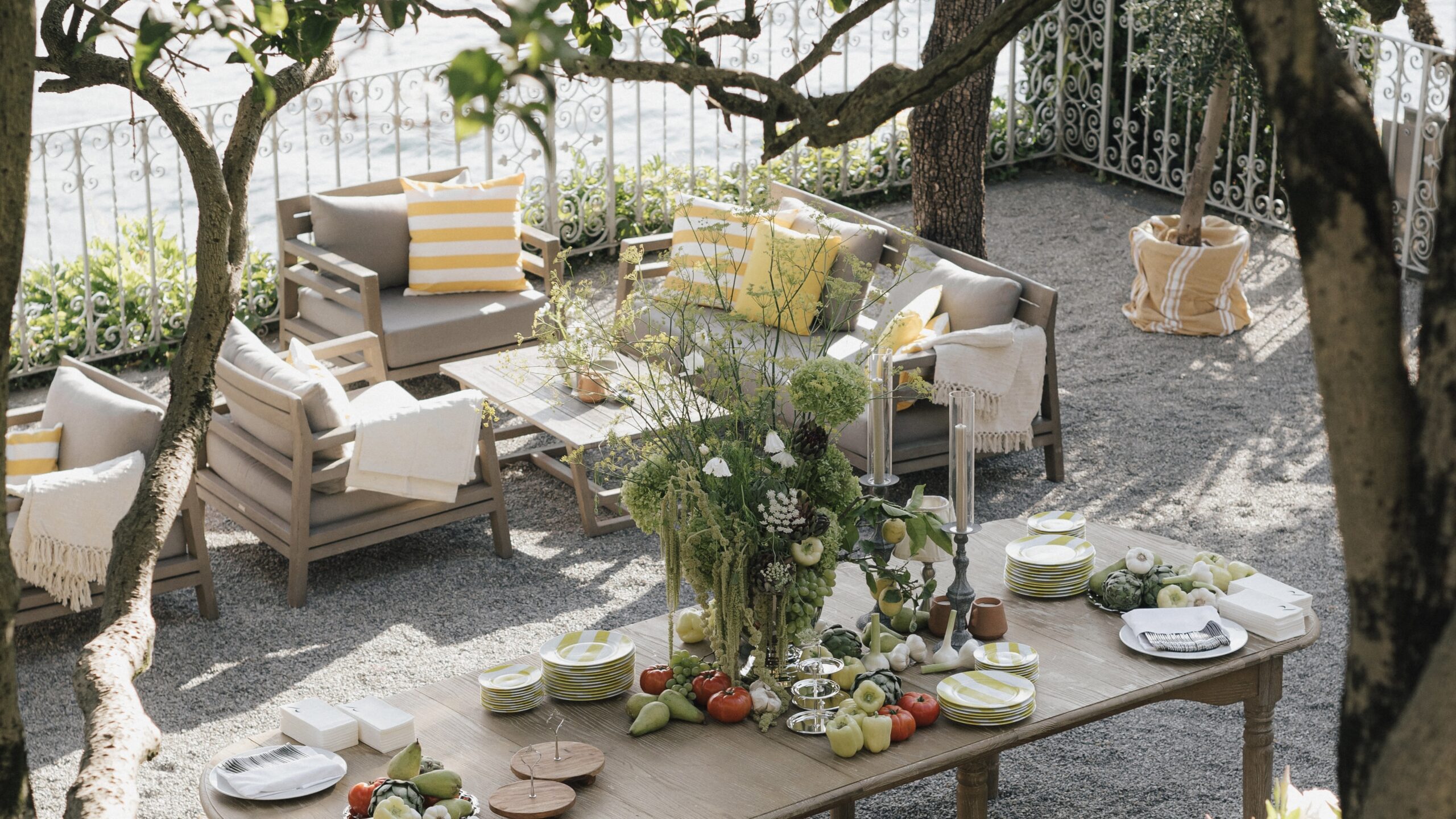 Gemütliche Lounge-Ecke auf einer Terrasse mit sommerlicher Dekoration, grünen Pflanzen und gelben Akzenten für eine Outdoor-Hochzeit.