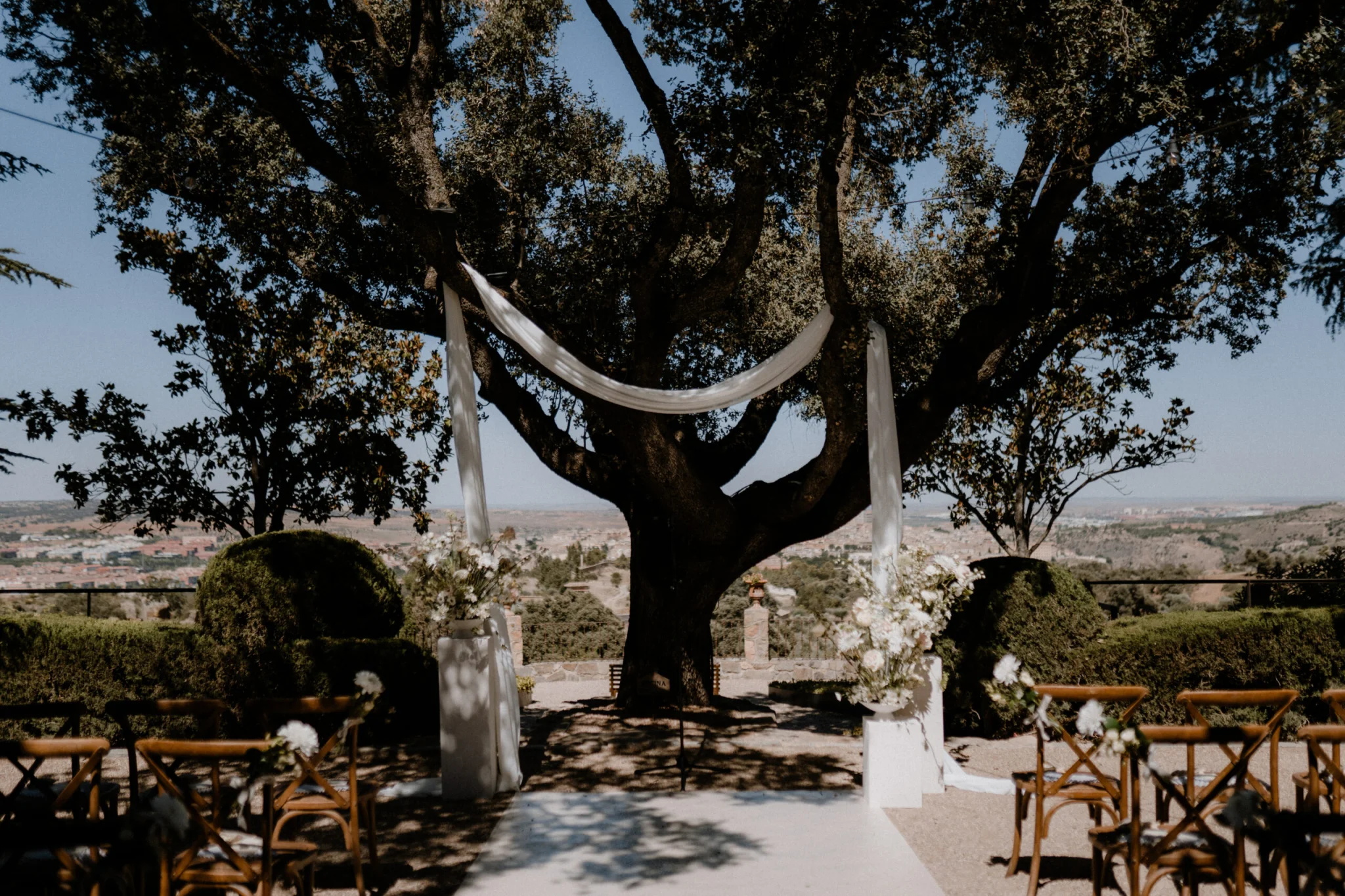 Idyllische Freiluft-Trauungszeremonie unter einem großen Baum mit weißem Dekorstoff und Blumenarrangements, perfekt für Hochzeiten im Freien in NRW.