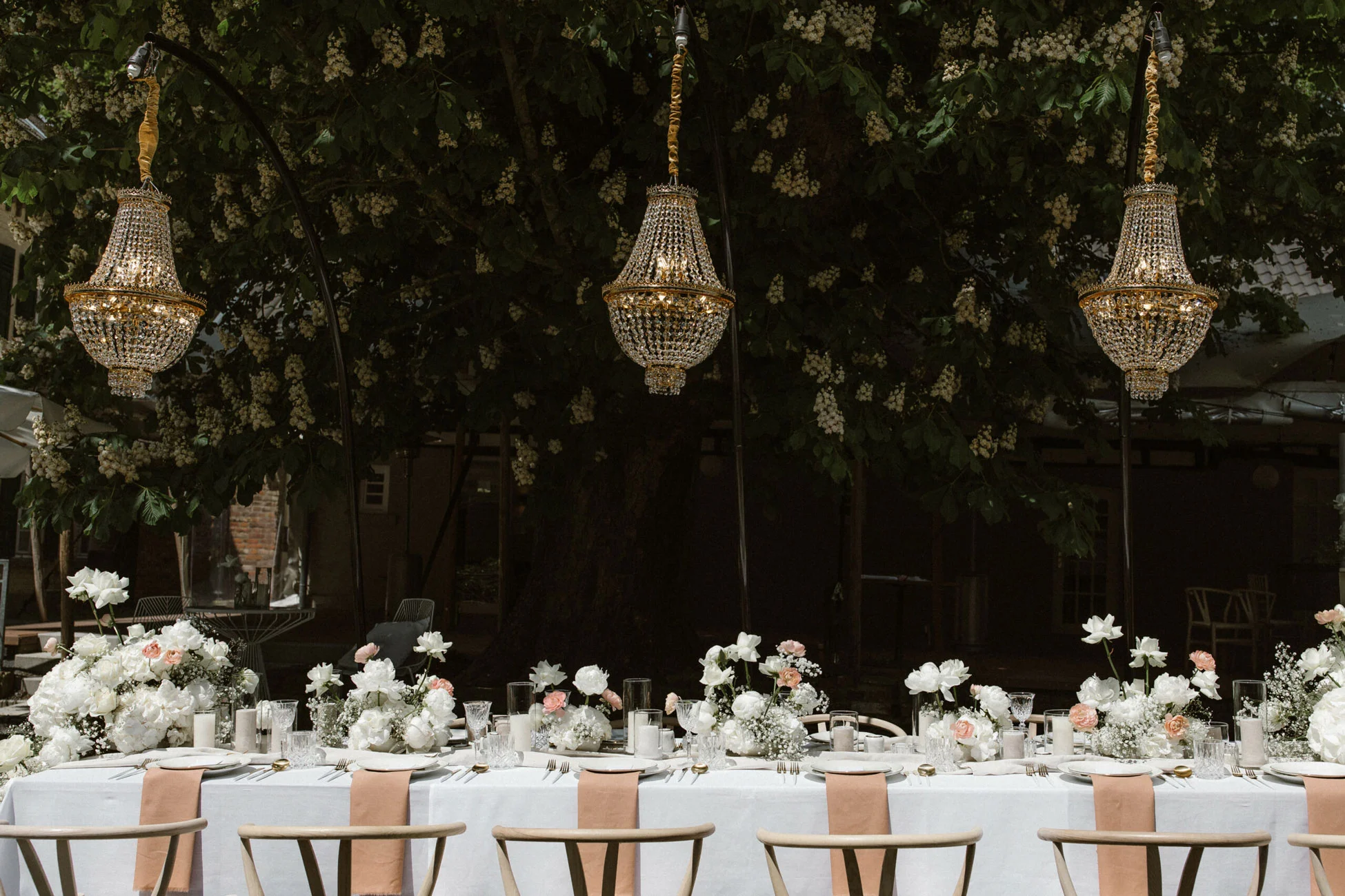 Goldenen Kristallkronleuchter hängen von von einem Baum über einem weißen Hochzeitstisch in Köln